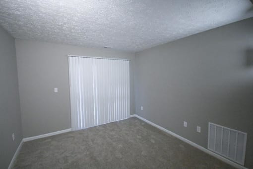 Empty living room with a large window and white blinds at Canterbury House apartments in Tipton, Indiana