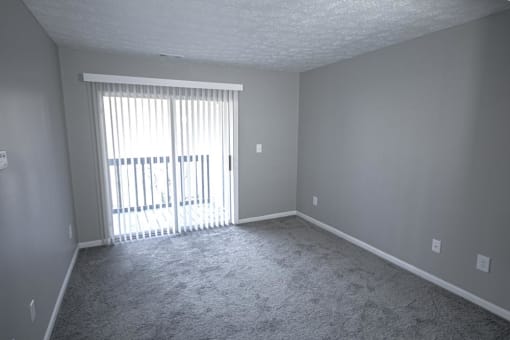 Empty living room with white walls and a sliding glass door and a carpeted floor at Canterbury House apartments in Logansport, Indiana