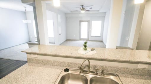 View from kitchen counter with sink with a living room with a door and window in the background at Mosaic Apartments in Avon, Indiana