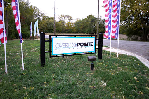 A sign that says Overlook Pointe Apartments in front of some flags.
