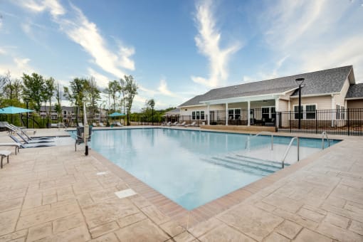 Swimming pool at Aurora Luxury Apartments with chaise lounge chairs and a building in the background