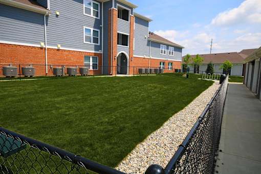 A grassy area in front of a building with a fence on the right side.