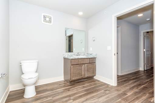 A white toilet sits in a bathroom with a wooden floor and a marble countertop.