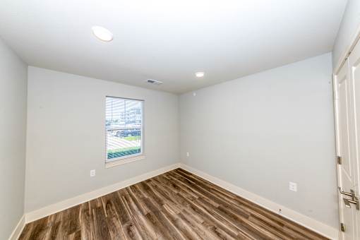 A room with wooden flooring and a window showing an outdoor view.