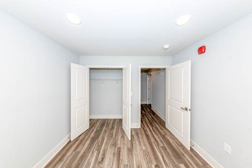 A room with a wooden floor and white walls, with a red fire alarm on the wall.
