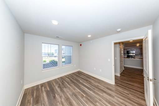 A room with wooden flooring and a view of a parking lot through the window.
