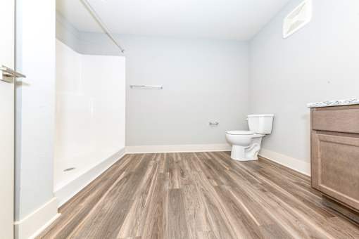 A white toilet sits in a bathroom with wood flooring.