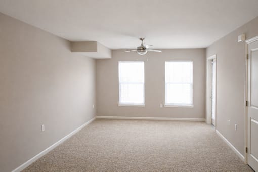 A room with a carpet floor, a ceiling fan, and two windows.