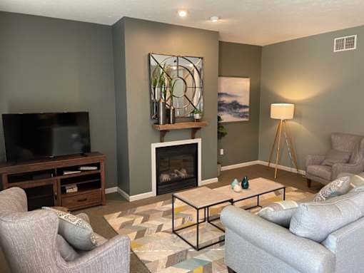 A living room with a grey couch, a grey armchair, a coffee table, a television, a fireplace, and a painting on the wall.