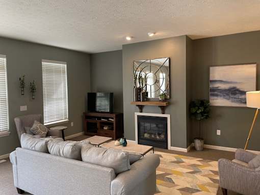 A living room with a grey couch, a fireplace, and a painting on the wall.