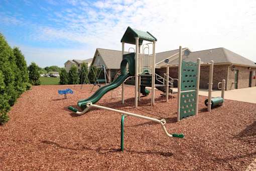 a childrens playground with a green swing set at Canterbury apartments in Kalamazoo, MI