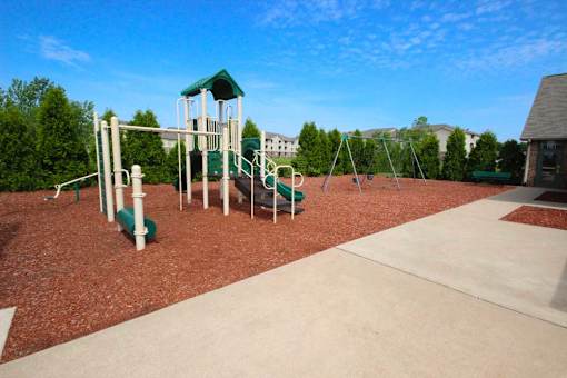 a childrens playground with a green swing set at Canterbury apartments in Kalamazoo, MI