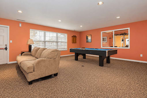 A room with a sofa, a table, and a pool table.