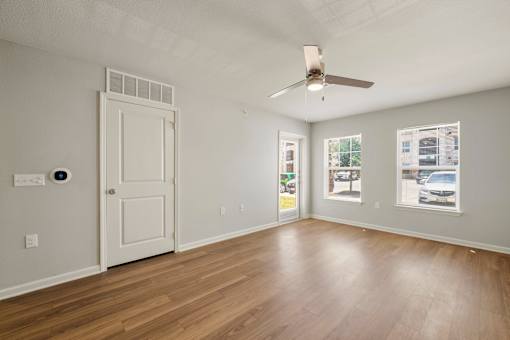 A room with a white door, a ceiling fan, and a window showing a parking lot outside.