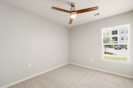 A room with a ceiling fan and a window showing a view of a parking lot.
