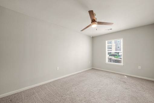 A room with a ceiling fan and a window showing a building outside.