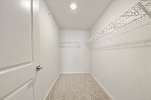 A white closet with a carpeted floor and a metal rack on the wall.
