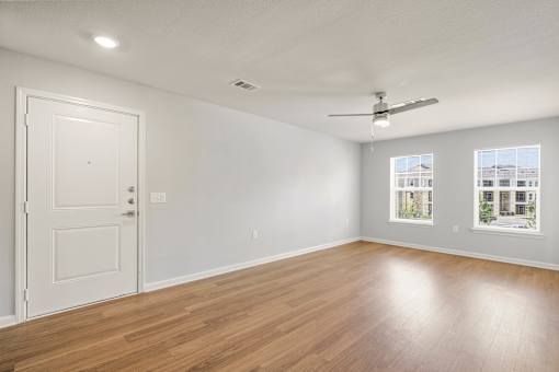 A room with a white door, a ceiling fan, and a window showing a building outside.