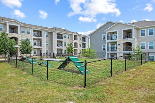 A playground area with a green slide and a fence in front of apartment buildings.