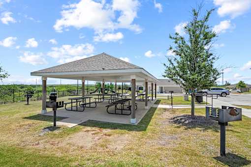 A pavilion with picnic tables is surrounded by a grassy area.