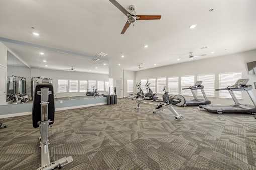 A spacious gym with a variety of exercise equipment and a ceiling fan.