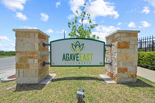 A green sign with the name "AGAVEEAST" is mounted on a stone pillar.