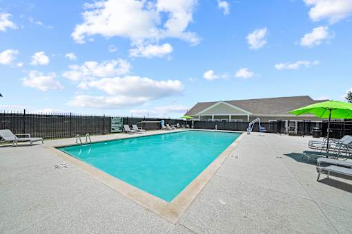 A large outdoor swimming pool with a green umbrella and lounge chairs.