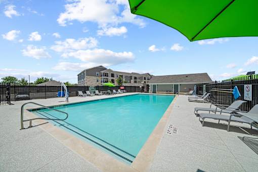 A pool with a green umbrella and chairs around it.