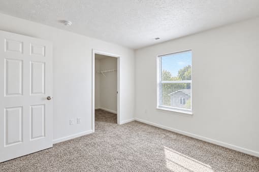 A room with a white door, carpeted floor, and a window with blinds.