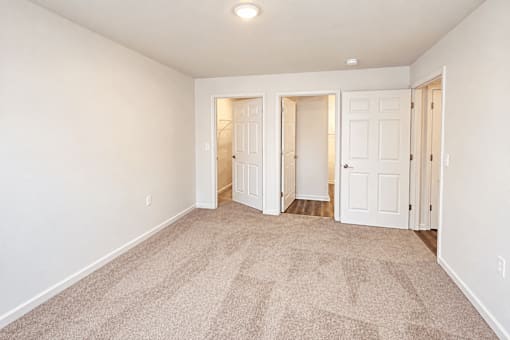 A room with carpeted floor and white walls with three doors.