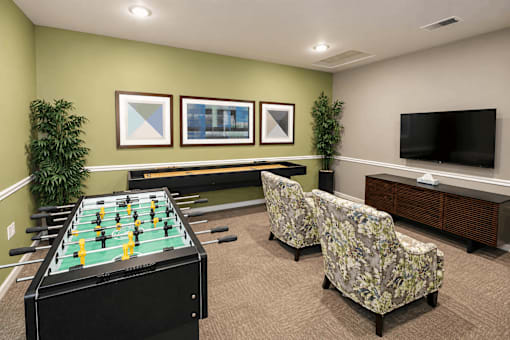 A foosball table is in the middle of a room with two chairs and a television.