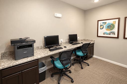 A room with a desk, two chairs, a monitor, a keyboard, and a printer.