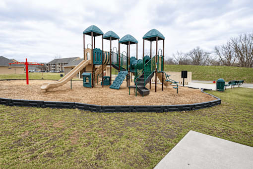 A playground with a green slide and a brown sandbox.