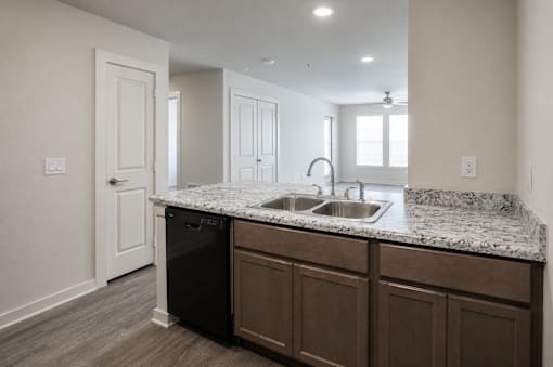 A kitchen with a black dishwasher and brown cabinets.