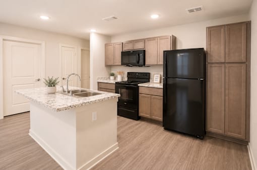 A kitchen with a black refrigerator and brown cabinets.