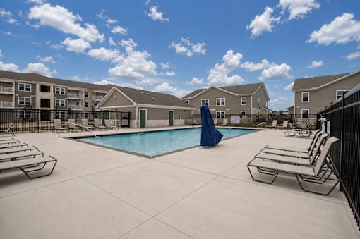 A swimming pool surrounded by lounge chairs and apartment buildings in the background.