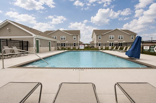 A swimming pool surrounded by lounge chairs in front of apartment buildings.