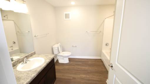 A white toilet sits in a bathroom with a sink and mirror.