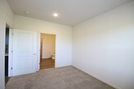 an empty living room with white walls and a door to a bathroom