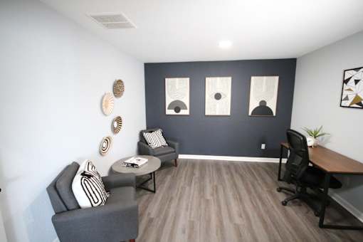 A room with a grey sofa, a black chair, a grey table and a wooden desk.