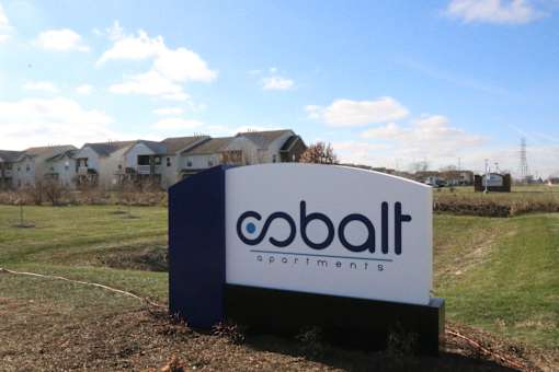 A Cobalt Apartments sign is in front of a grassy area with houses in the background.