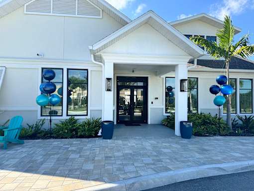 A white house with a black door and windows, surrounded by plants and blue balloons.