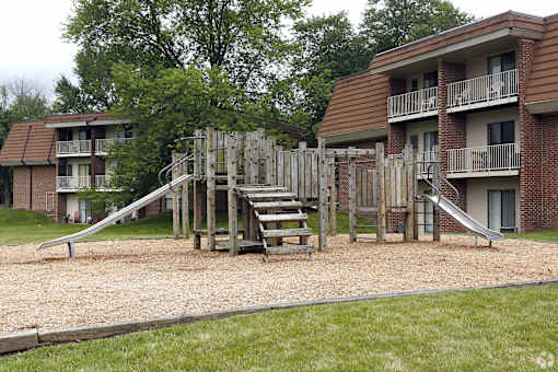 A playground with a slide and a wooden structure in front of apartment buildings.