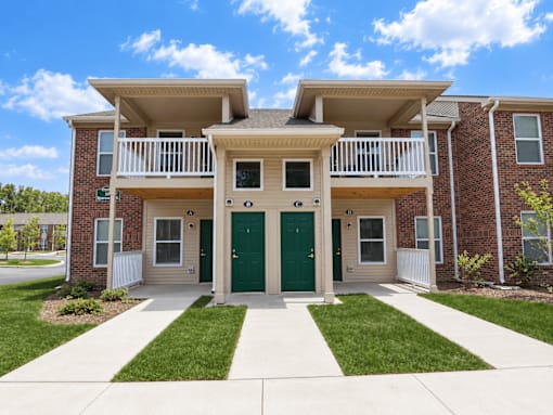 A two-story brick apartment building with a green door and white railings.