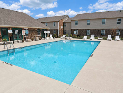 A swimming pool surrounded by lounge chairs and apartment buildings.