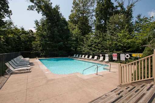 A pool surrounded by trees and chairs.