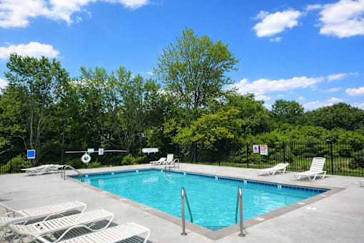 A pool surrounded by trees and chairs.