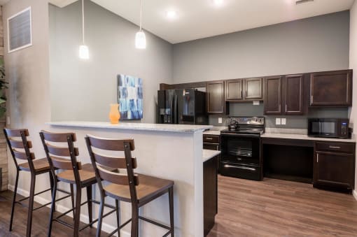 Clubhouse kitchen with 3 barstools and cabinets and black appliances at Mosaic Apartments in Avon, Indiana
