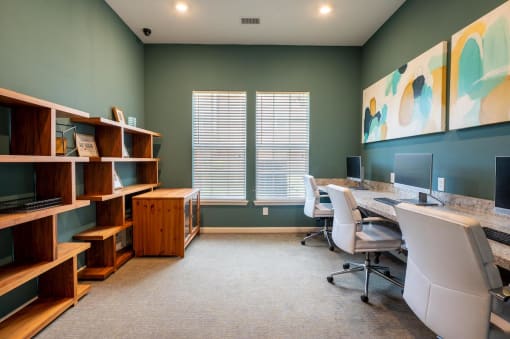 Small room with a book shelf and a long desk with computer monitors and chairs with 2 windows at Mosaic Apartments in Avon, Indiana