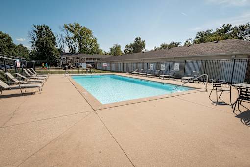 A large outdoor swimming pool surrounded by sun loungers and a building in the background.